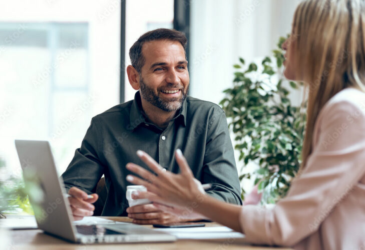 Séance de coaching en entreprise avec un homme souriant écoutant activement une collègue, démontrant l'approche personnalisée et l'engagement d'Axis Mundi envers le développement professionnel.
