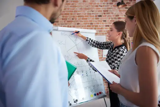 Formation management d'équipe : formatrice expliquant une stratégie organisationnelle sur tableau blanc devant un groupe de collaborateurs