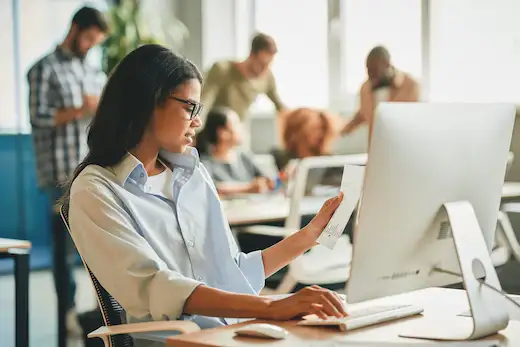 Formation PSSM - Premiers Secours en Santé Mentale : professionnelle consultant un document devant son ordinateur dans un environnement de travail en open space